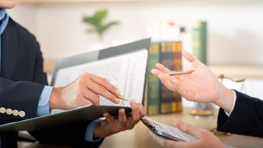 Un hombre con traje sostiene un papel en sus manos, mostrando una expresión seria y concentrada.