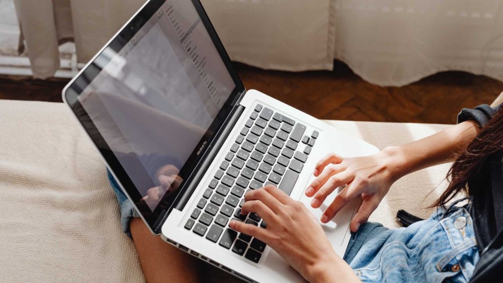 Mujer sentada en un sofá, usando su laptop con una expresión concentrada.