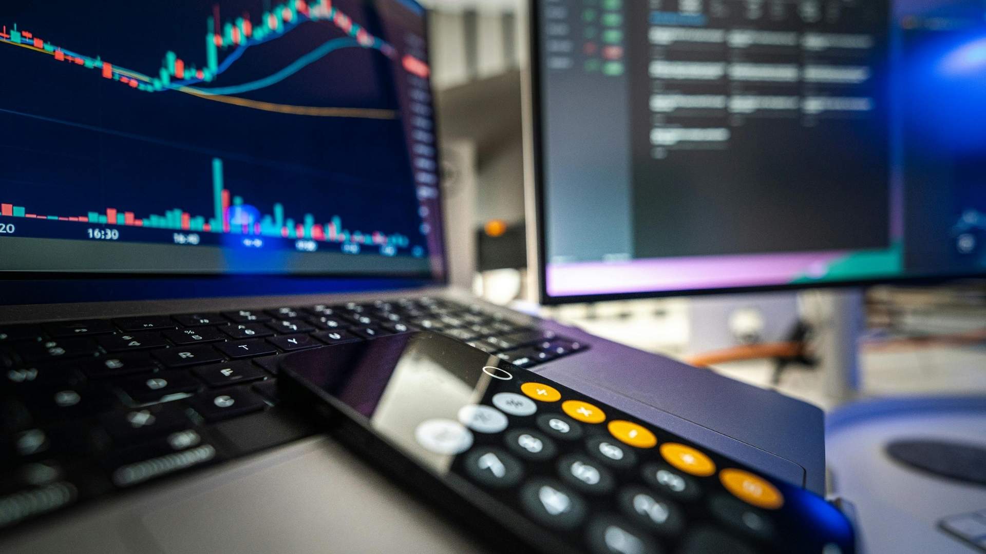 Gráfico del mercado de valores en una laptop junto a una calculadora sobre una mesa.