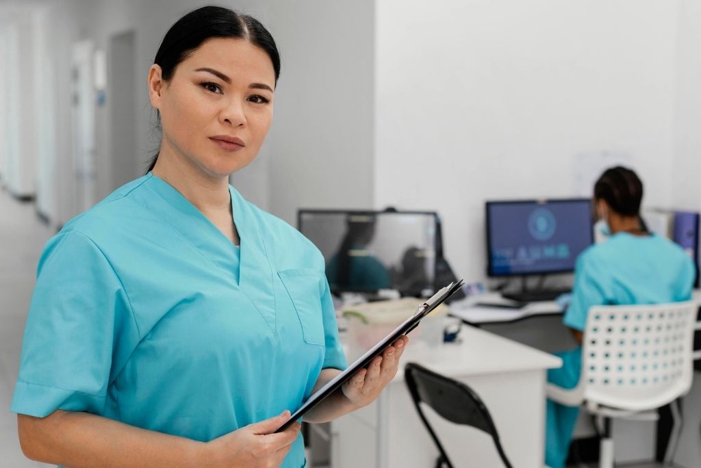 Profesional de salud con portapapeles frente a estación de trabajo con computador en clínica colombiana
