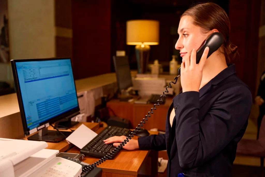 Recepcionista de hotel gestionando reservas en computador con sistema PMS.