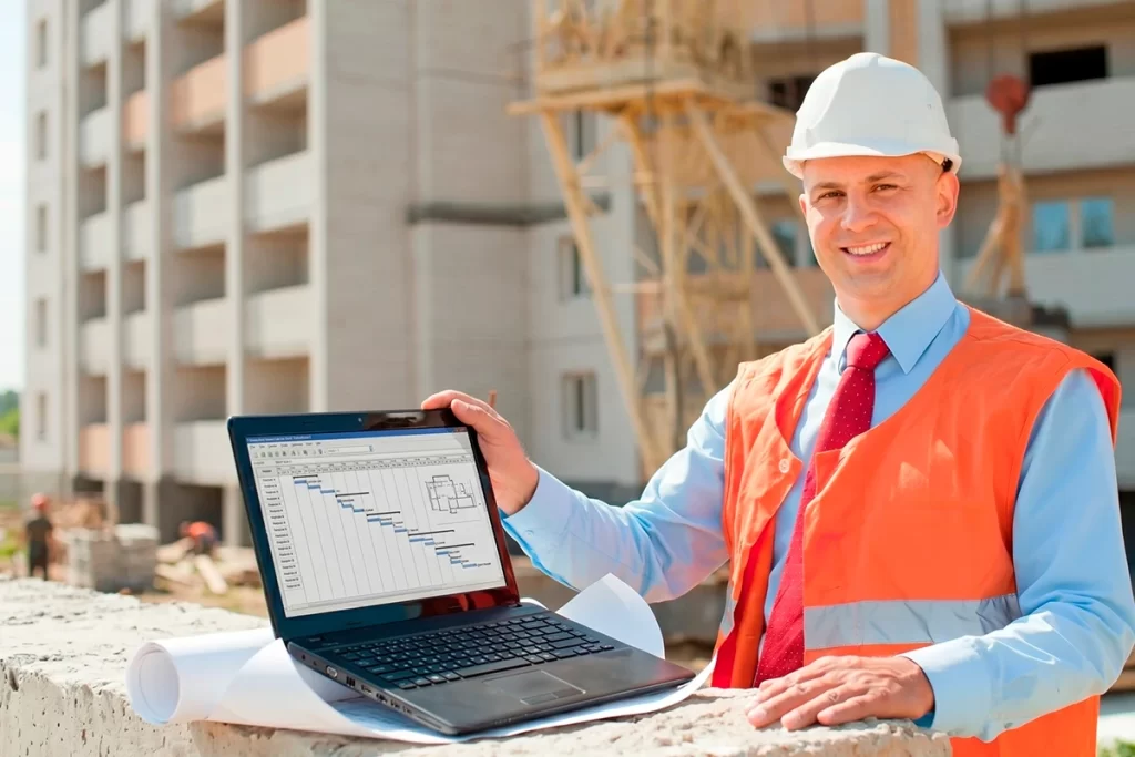 Ingeniero en obra de construcción usando laptop con software de gestión de proyectos.