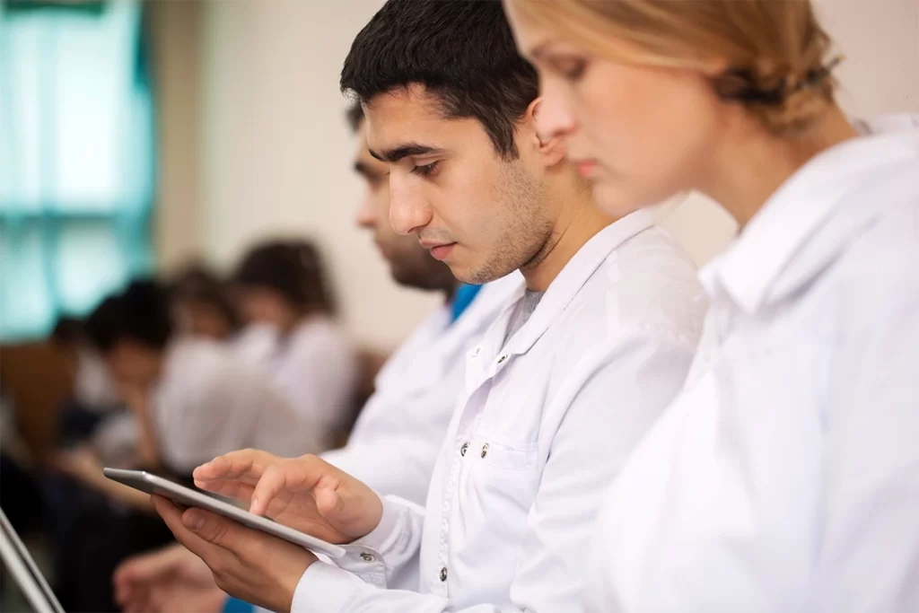 Profesionales de la salud en bata blanca revisando información en tablets digitales durante una conferencia.
